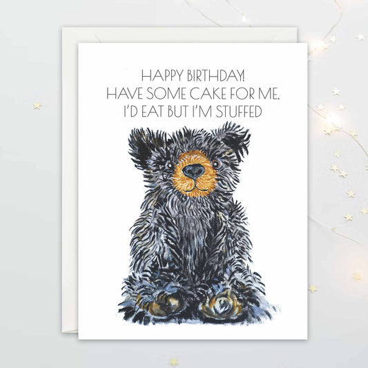 Birthday card with a teddy bear illustration and humorous text on a white background: "Happy Birthday! Have some cake for me. I'd eat but I'm stuffed"