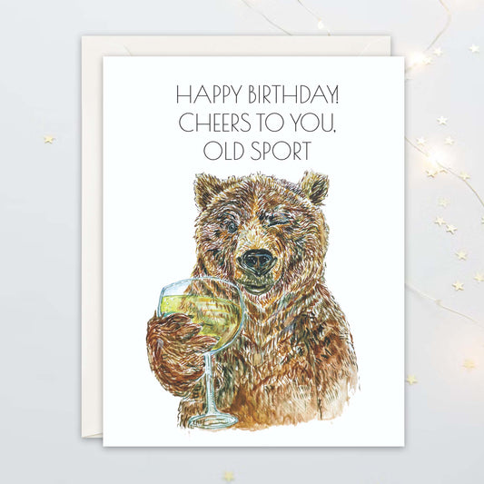 Birthday card with bear holding a glass of wine and text 'Happy Birthday, Cheers to You, Old Sport' on a white background.
