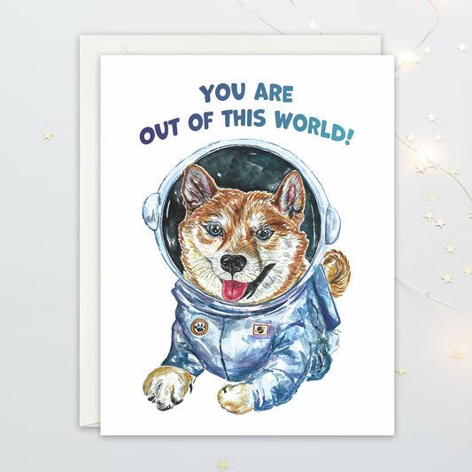 Watercolour illustrated greeting card of a Shiba Inu puppy in a space suit with 'You are out of this world!' text on a white background.
