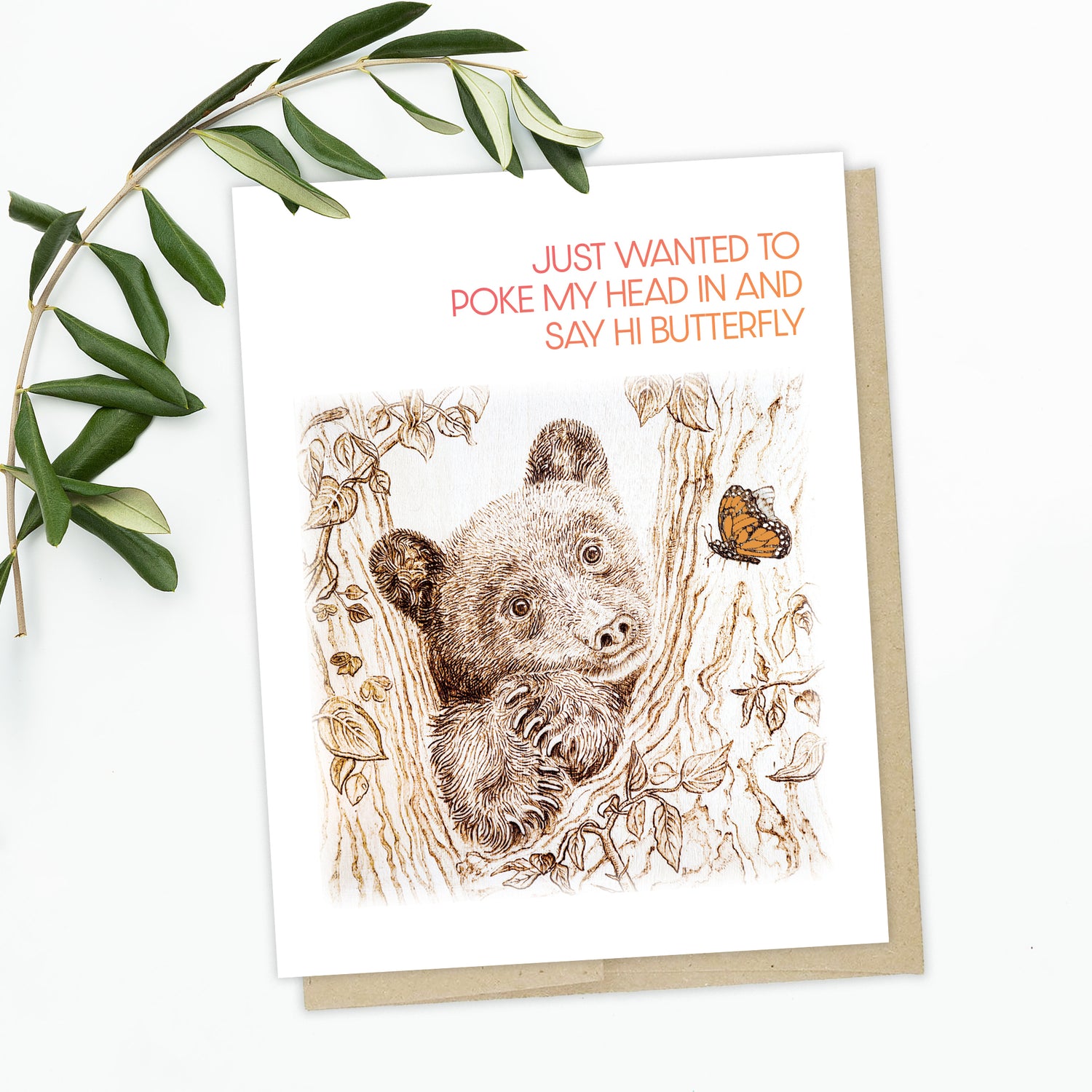 A "Just Because" Card with a pyrography art hand drawn bear poking his head and paws out in between lush trees, checking in on a monarch butterfly. Text reads "Just Wanted to poke my head in and say hi butterfly"