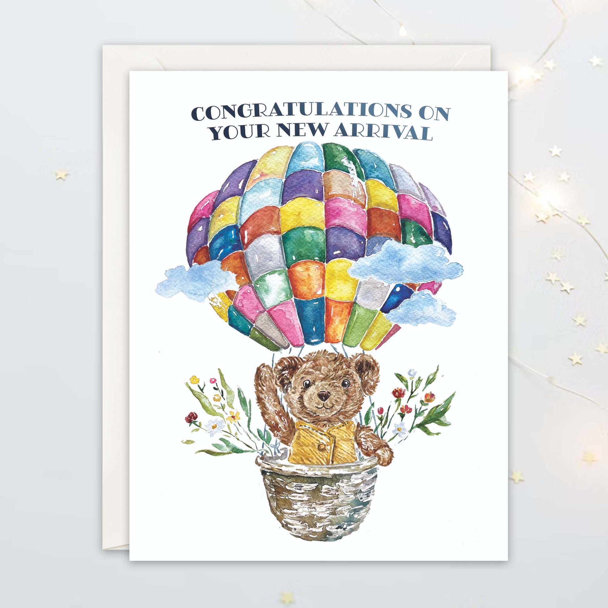 Greeting card with a teddy bear in a hot air balloon and text 'Congratulations on your new arrival' on a white background.
