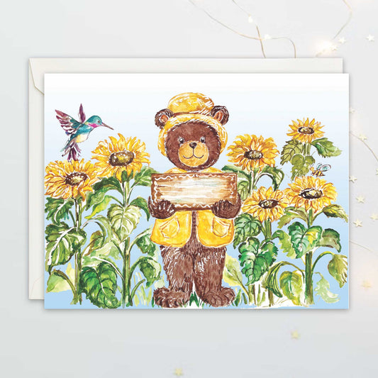 Greeting card with a bear holding a sign among a sunflowers field. The sign is blank for customization
