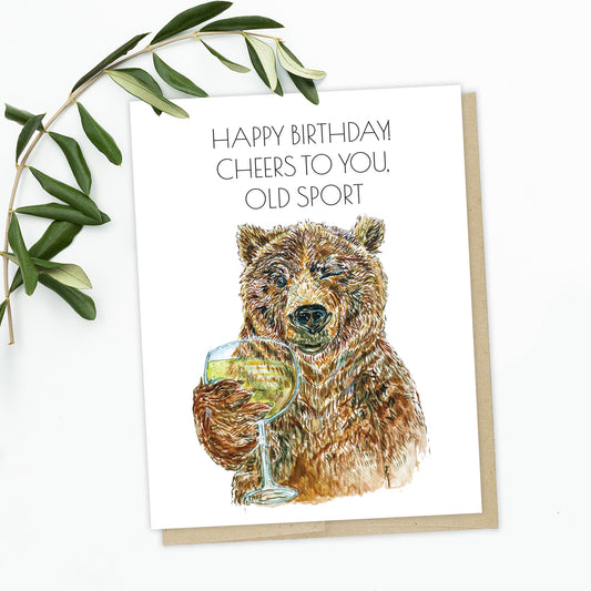 A birthday card featuring a brown, grizzly bear holding out a glass of champagne. The bear is winking and his expression is like Jay Gatsby from the party scene of the Great Gatsby movie. The text reads: Happy Birthday! Cheers to You, Old Sport.