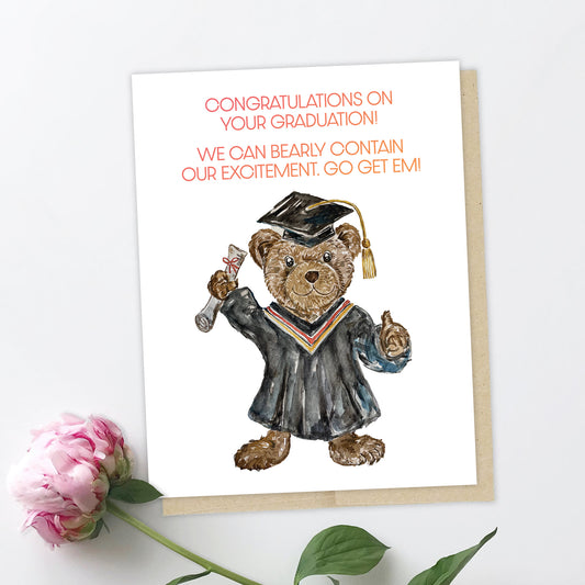 An image of a greeting card with a pink peony. The card features a brown bear dressed in a graduation gown and wearing the square black graduation cap. She is holding a diploma in one paw, and giving the thumbs up gesture with the other paw. The text reads: Congratulations on your graduation! We can "bearly" contain our excitement. Go get em!