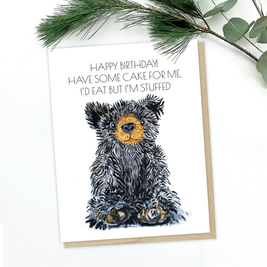 A picture of a teddy bear greeting card. The bear is black with perky ears, a brown snout and brown/white paws. The text reads: happy birthday! have some cake for me. I'd eat but I'm stuffed.